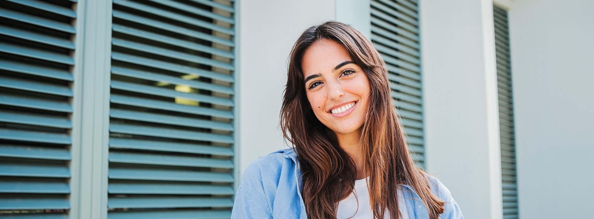 The image is a photograph of a woman with light skin, smiling at the camera. She appears to be in her late twenties or early thirties and has long hair. Her eyes are looking directly at the camera, and she is holding up her index finger near her mouth as if she s making a point or emphasizing something. The background is plain and light-colored, which suggests that this could be a stock photo used for various purposes such as advertising, personal branding, or lifestyle content.