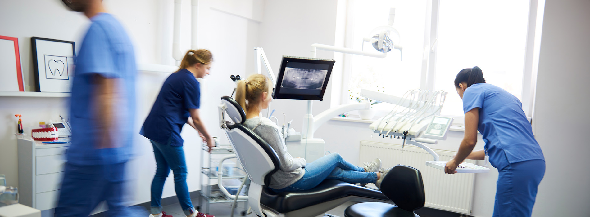 A group of healthcare professionals in a dental office, with one individual seated at a computer workstation and others standing around the room.