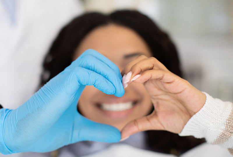 A person wearing a blue surgical gown and gloves is holding a heart-shaped object in front of their face.
