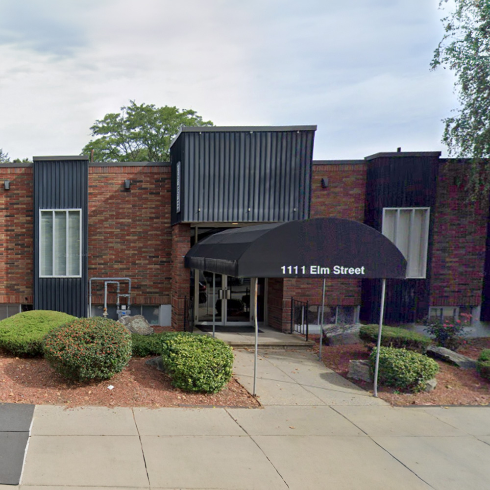 The image is a photograph of a brick building with two visible storefronts, one of which has a sign that reads  111 Elm Street.  There are no people in the immediate vicinity.