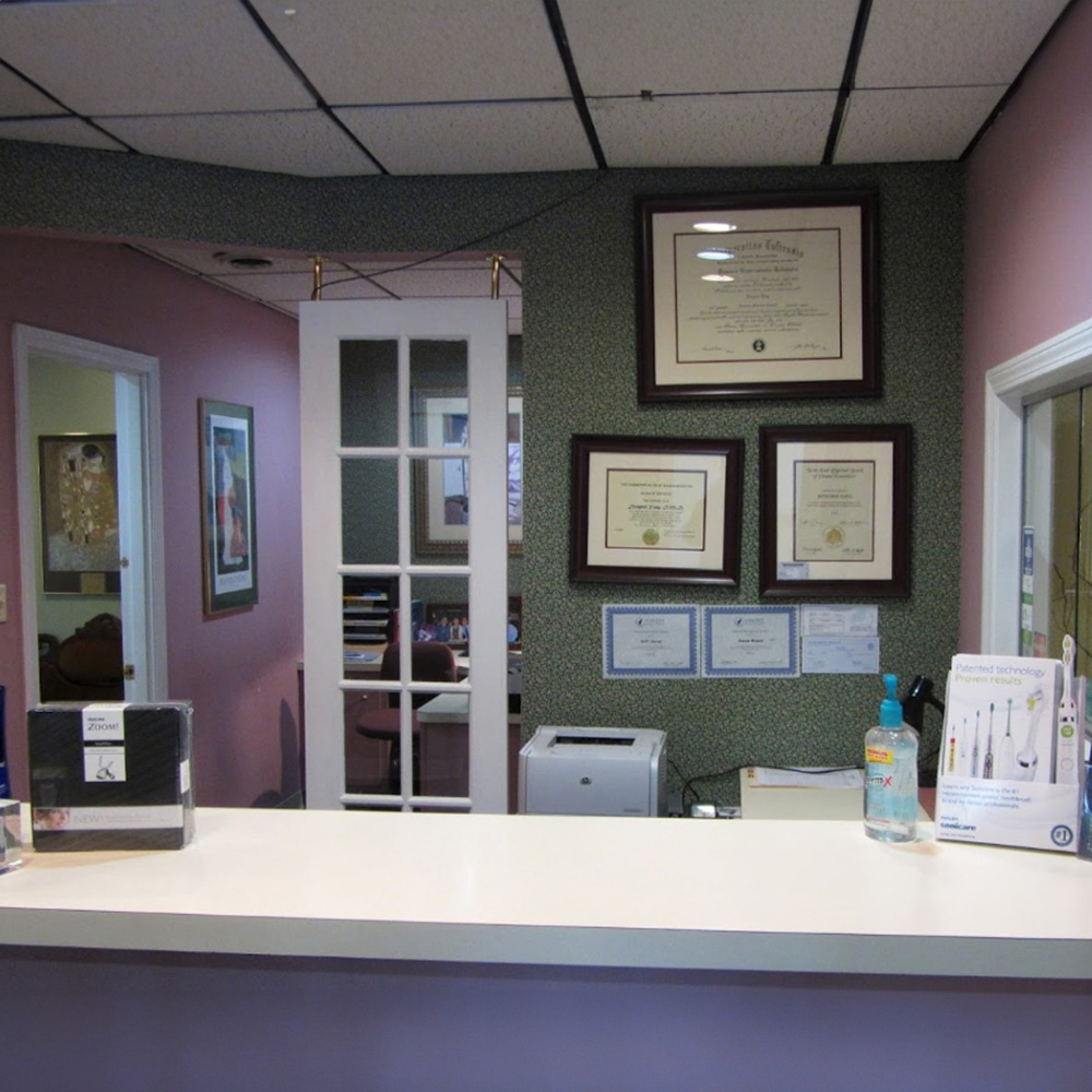 The image shows an interior view of a room with a framed diploma on the wall, two framed certificates hanging above a counter, and a white countertop with various items on it.